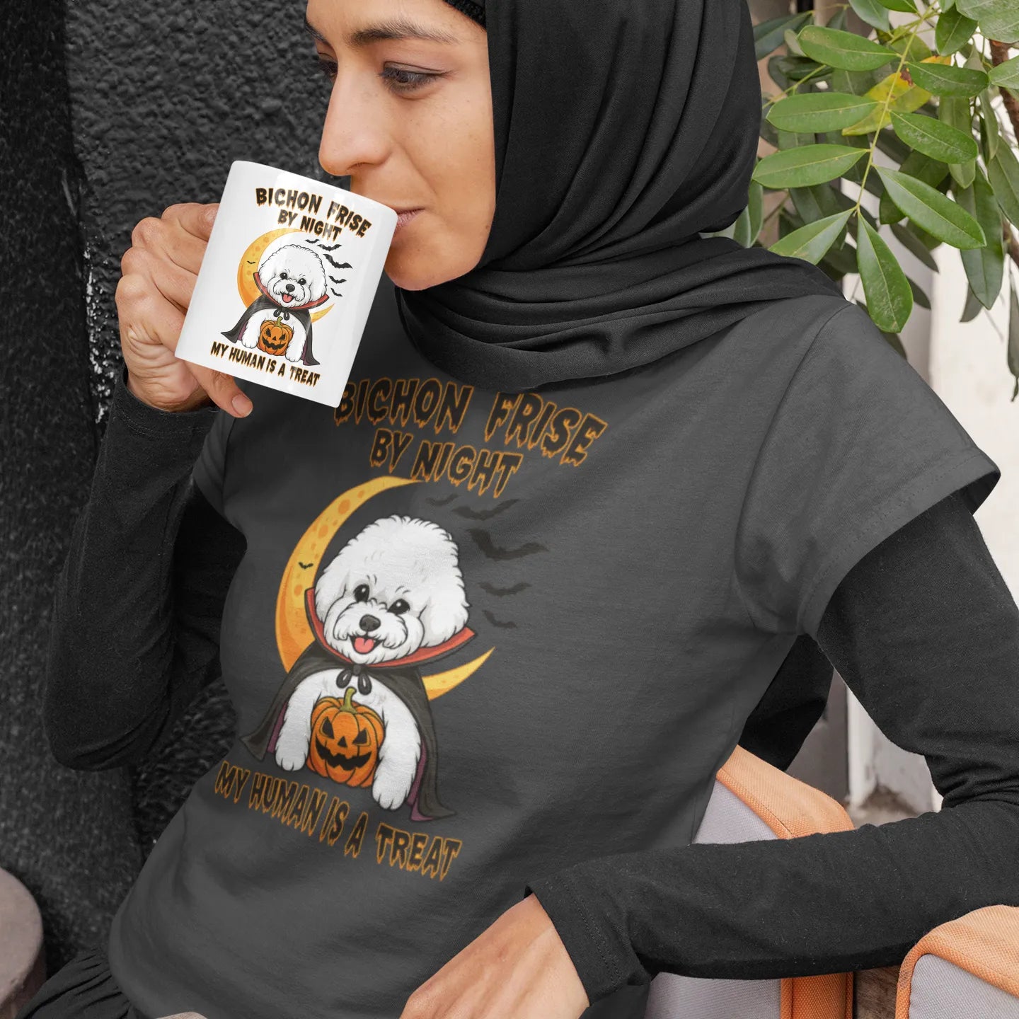 Muslim woman in hijab enjoying coffee from a Halloween-themed mug featuring a cute Bichon Frise in vampire costume, matching T-shirt design, perfect gift for dog lovers and spooky season fans.