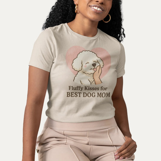 Smiling woman wearing a beige “Fluffy Kisses for the Best Dog Mom” Bichon Frise t-shirt, sitting indoors in a modern room – perfect for proud dog moms