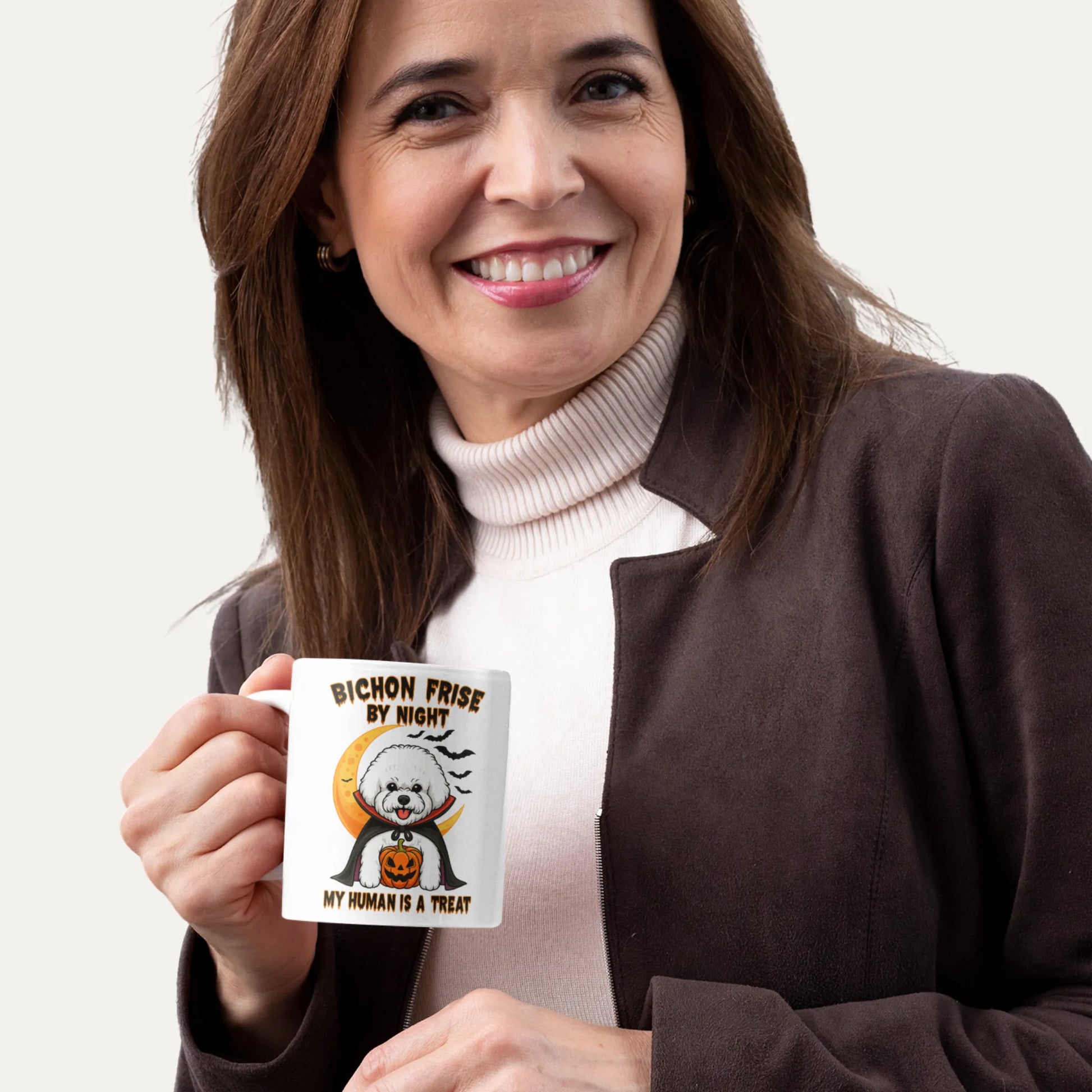 Smiling woman holding a white Halloween coffee mug with a Bichon Frise vampire design and the text "Bichon Frise by Night – My Human is a Treat