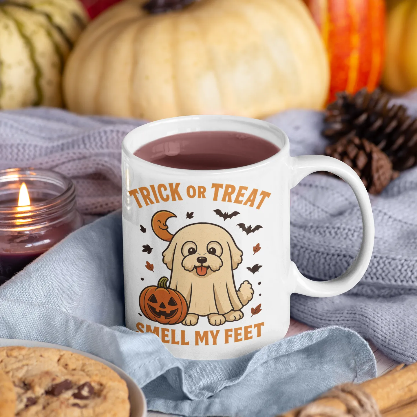 White ceramic Halloween mug with Bichon Frise ghost design and "Trick or Treat Smell My Feet" quote, surrounded by autumn decorations, pumpkins, pinecones, and cozy textures – perfect for fall gifting.