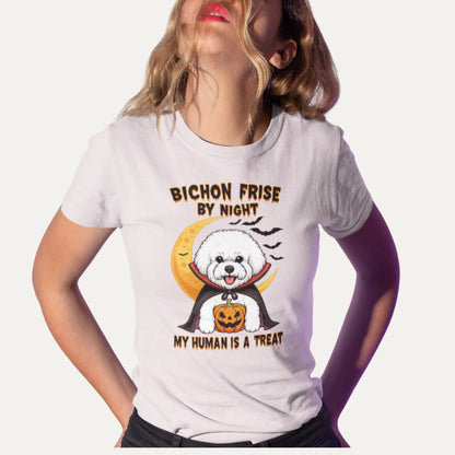 Woman wearing a white T-shirt with a Halloween-themed design of a Bichon Frise dressed as a vampire holding a pumpkin. The shirt text reads “Bichon Frise by Night – My Human Is a Treat”. Purple shadow background