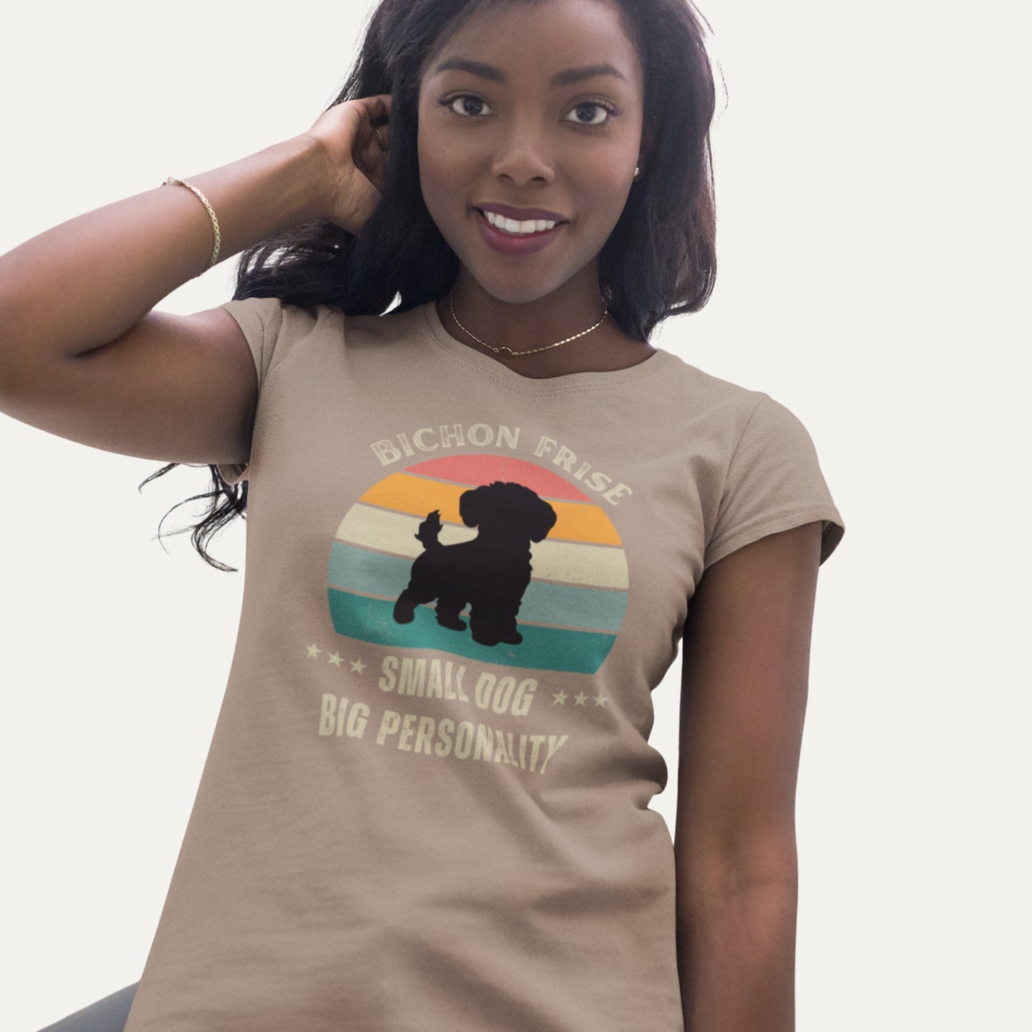 Woman wearing a retro-style beige T-shirt with 'Bichon Frise – Small Dog, Big Personality' design featuring a silhouette of a Bichon Frise in front of a vintage sunset graphic.
