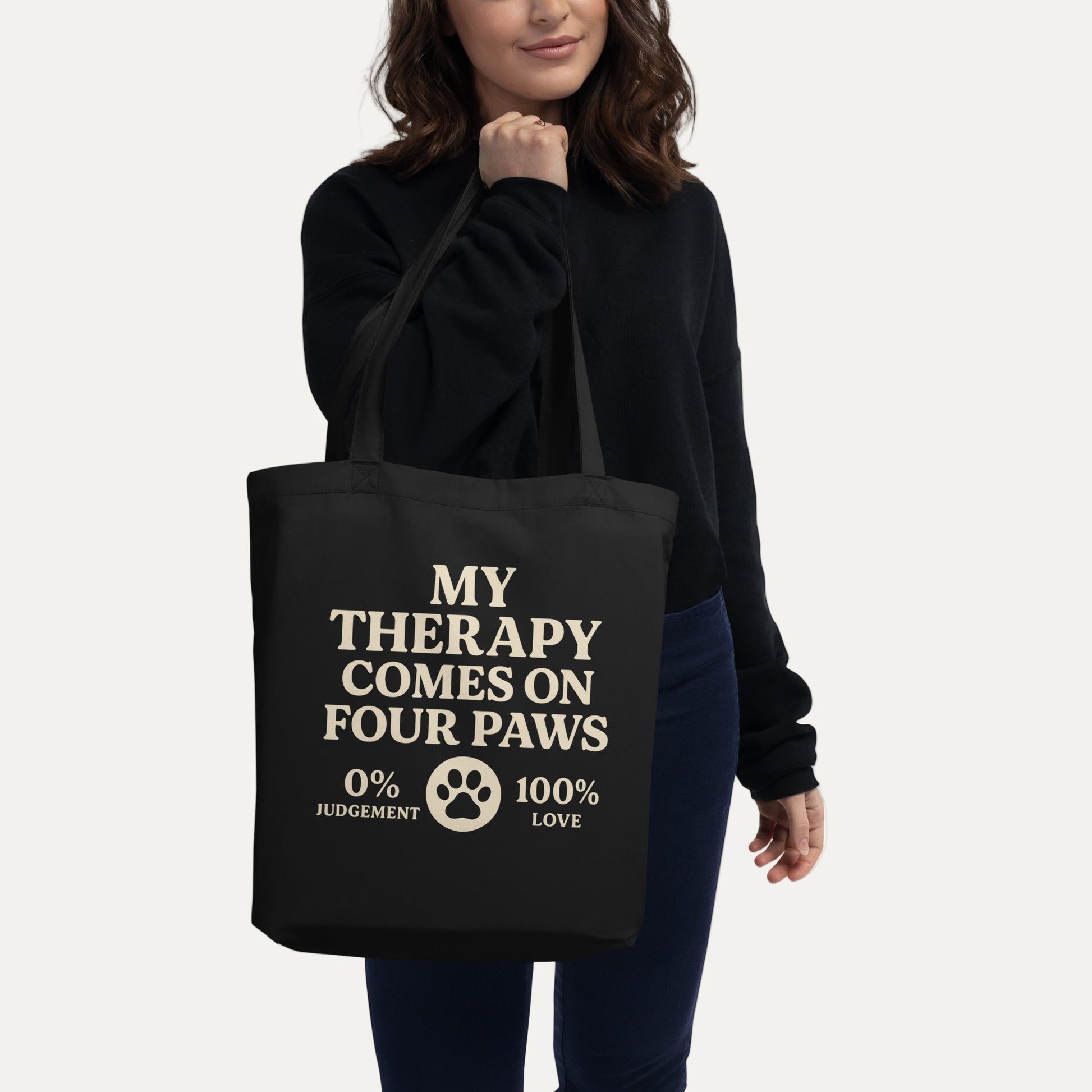 Woman holding a black eco-friendly tote bag with ‘My Therapy Comes on Four Paws’ text and paw print design – Fun Factory Frise.