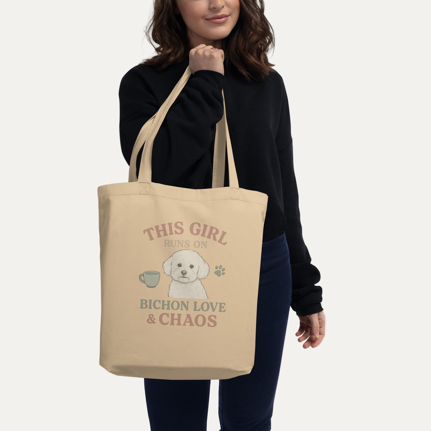 Woman holding beige eco tote bag with funny Bichon Frise dog print and text This Girl Runs on Bichon Love & Chaos