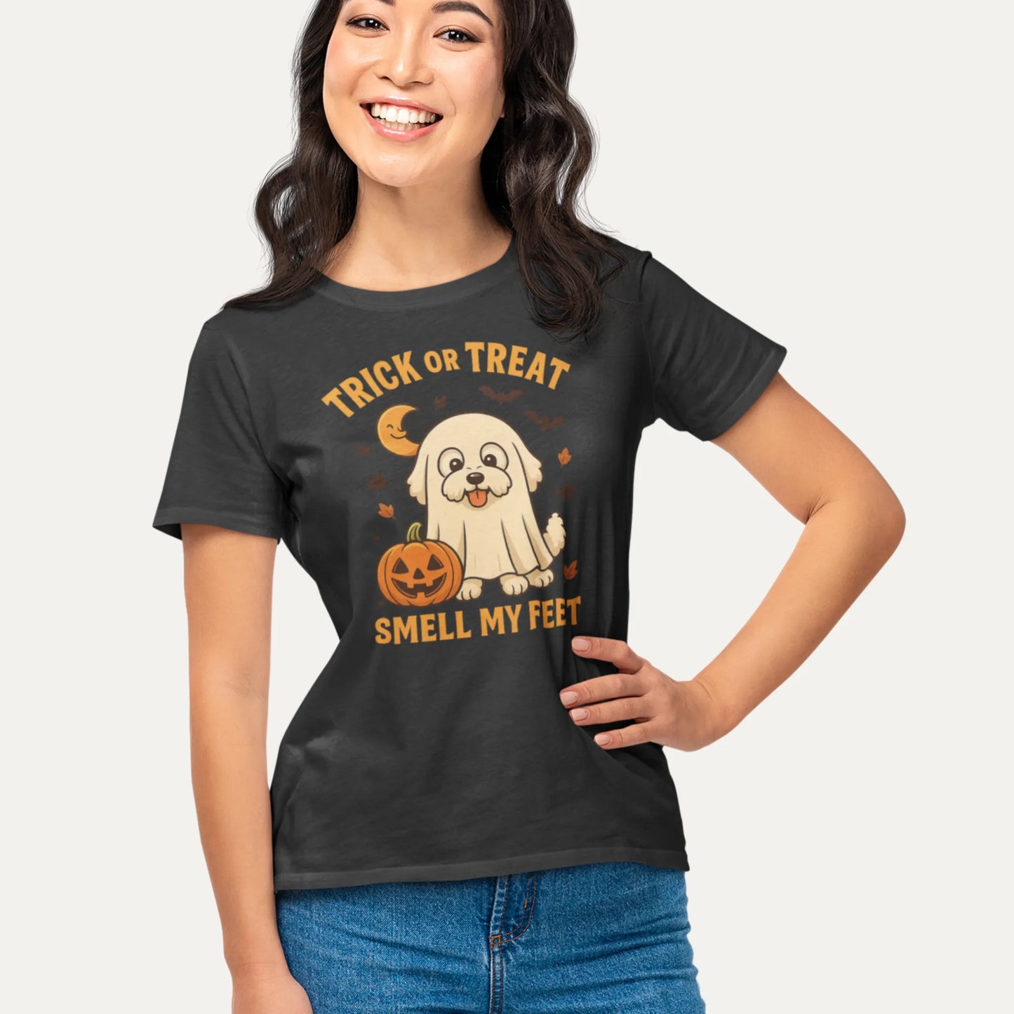Smiling woman wearing a black Halloween t-shirt with a cute Bichon Frise dressed as a ghost and pumpkin, featuring the text 'Trick or Treat Smell My Feet'

