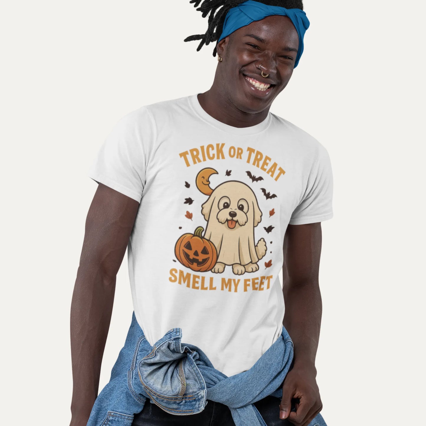 Smiling man wearing a white Halloween t-shirt featuring a cute Bichon Frise dressed as a ghost with a pumpkin and the text 'Trick or Treat Smell My Feet'
