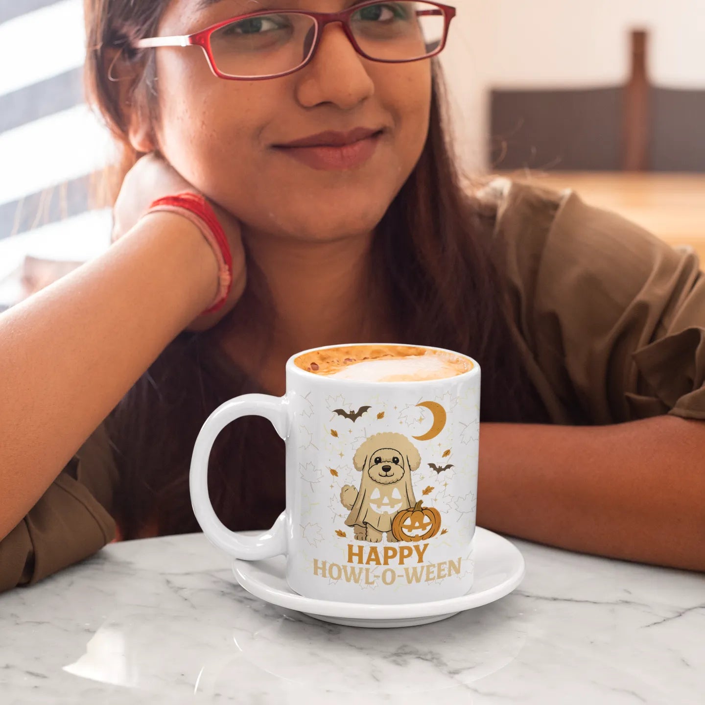 Smiling woman enjoying coffee at a cafe, holding a white ceramic mug with cute Halloween Bichon Frise ghost dog design and "Happy Howl-o-Ween" text – perfect spooky season gift for dog lovers