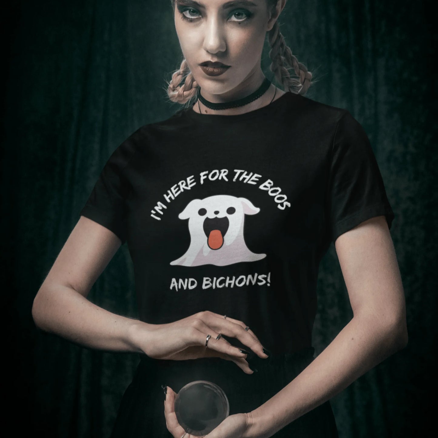 Gothic woman holding a crystal ball while wearing a Halloween T-shirt featuring a cute Bichon Frise ghost with the funny phrase “I’m here for the Boos and Bichons!