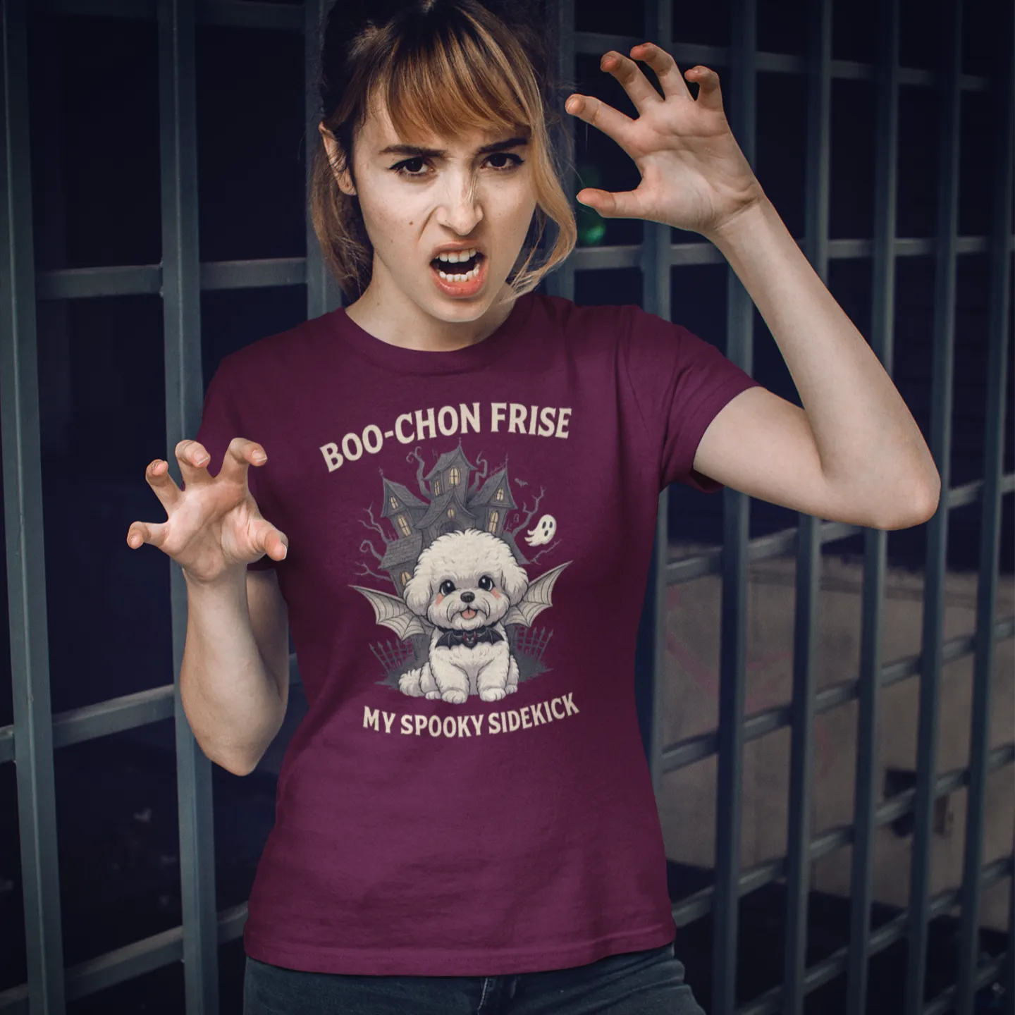 A woman modeling a maroon Halloween t-shirt for Bichon Frise lovers. The funny design features a Bichon Frise dog with bat wings and the text "BOO-CHON FRISE MY SPOOKY SIDEKICK